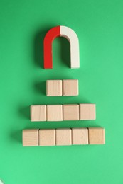 Photo of Magnet attracting wooden cubes on green background, flat lay