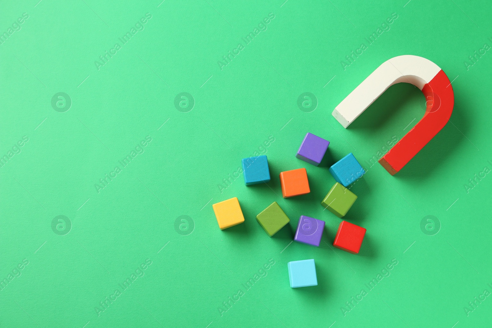 Photo of Magnet attracting colorful cubes on green background, flat lay. Space for text