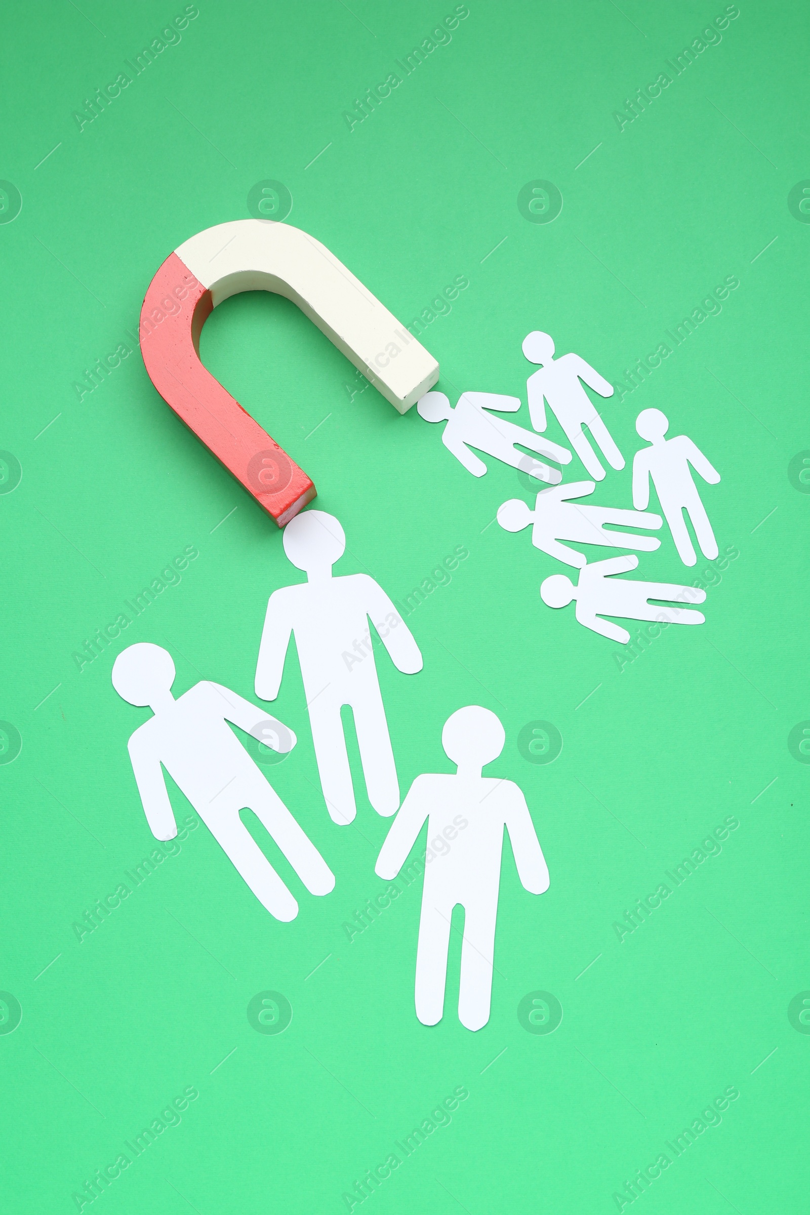 Photo of Magnet attracting paper people on green background, flat lay