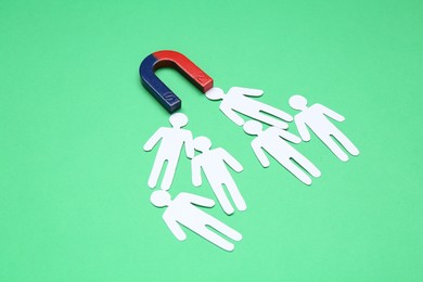 Photo of Magnet attracting paper people on green background