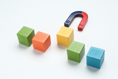 Photo of Magnet attracting colorful cubes on white background, closeup