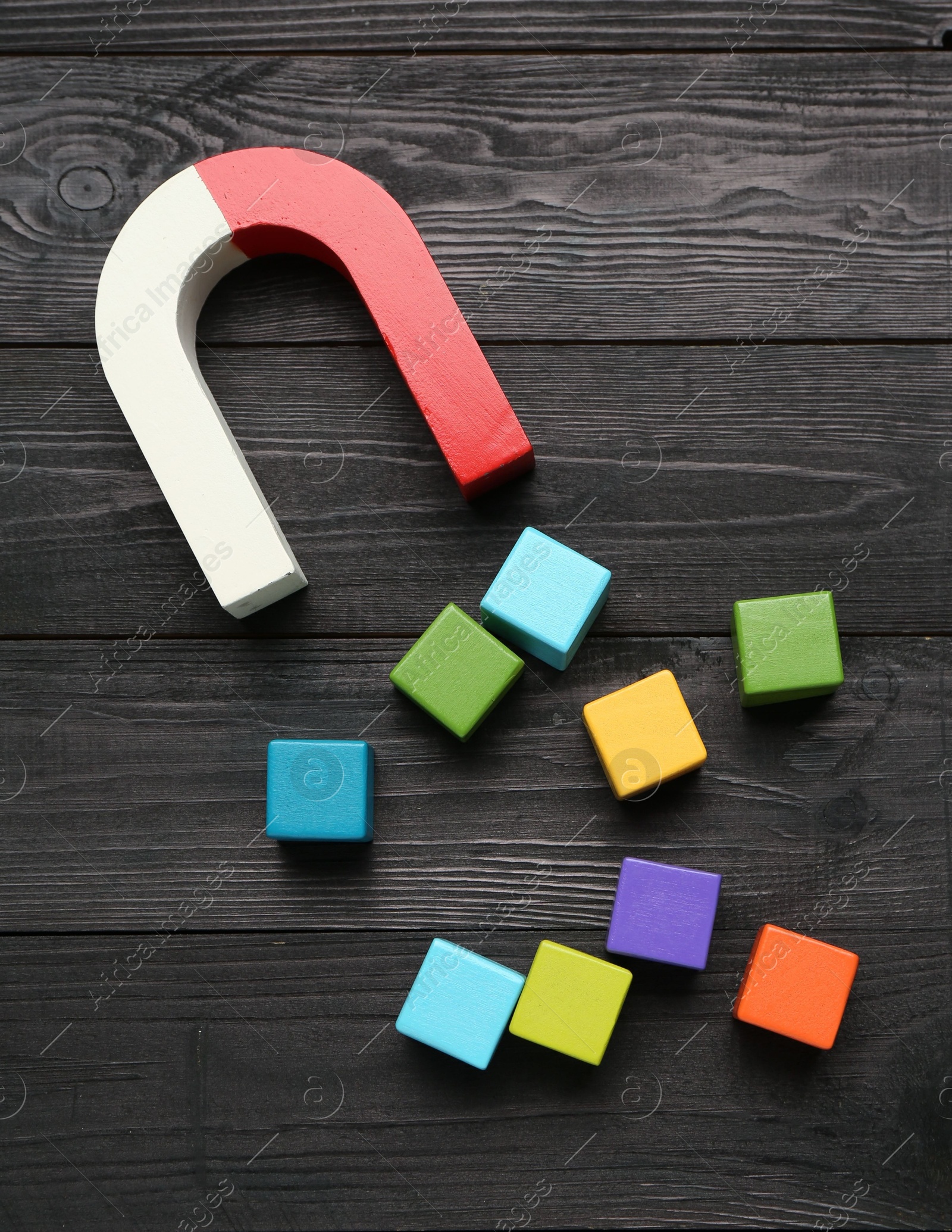 Photo of Magnet attracting colorful cubes on wooden table, flat lay