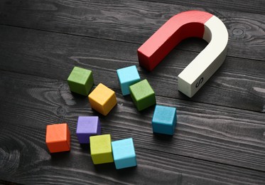 Photo of Magnet attracting colorful cubes on wooden table