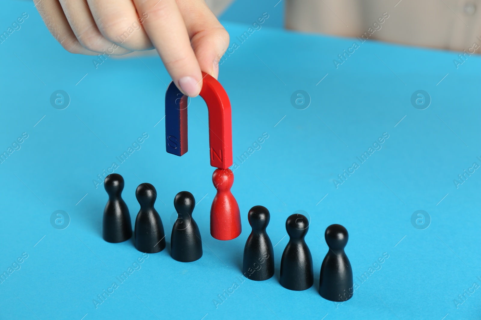 Photo of Woman with magnet attracting red piece among black ones on light blue background, closeup