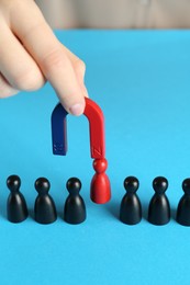 Photo of Woman with magnet attracting red piece among black ones on light blue background, closeup