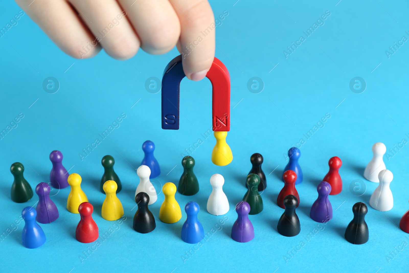 Photo of Woman with magnet attracting yellow piece among colorful ones on light blue background, closeup