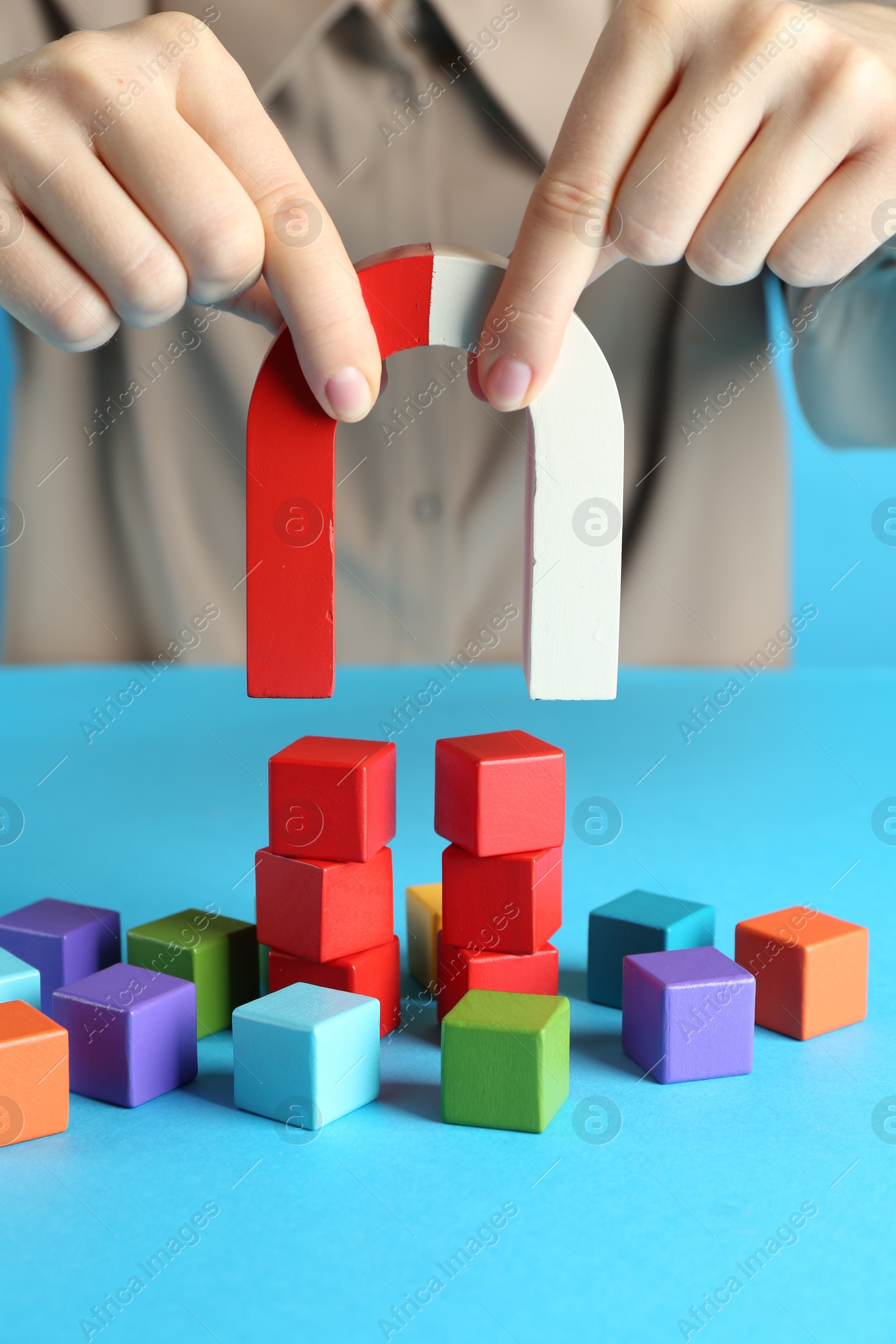 Photo of Woman with magnet attracting colorful cubes on light blue background, closeup