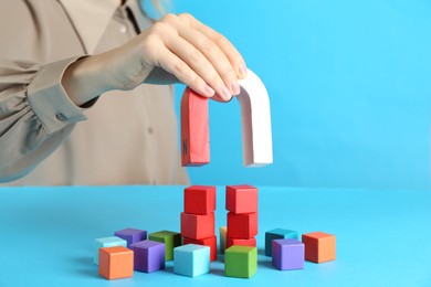 Photo of Woman with magnet attracting colorful cubes on light blue background, closeup