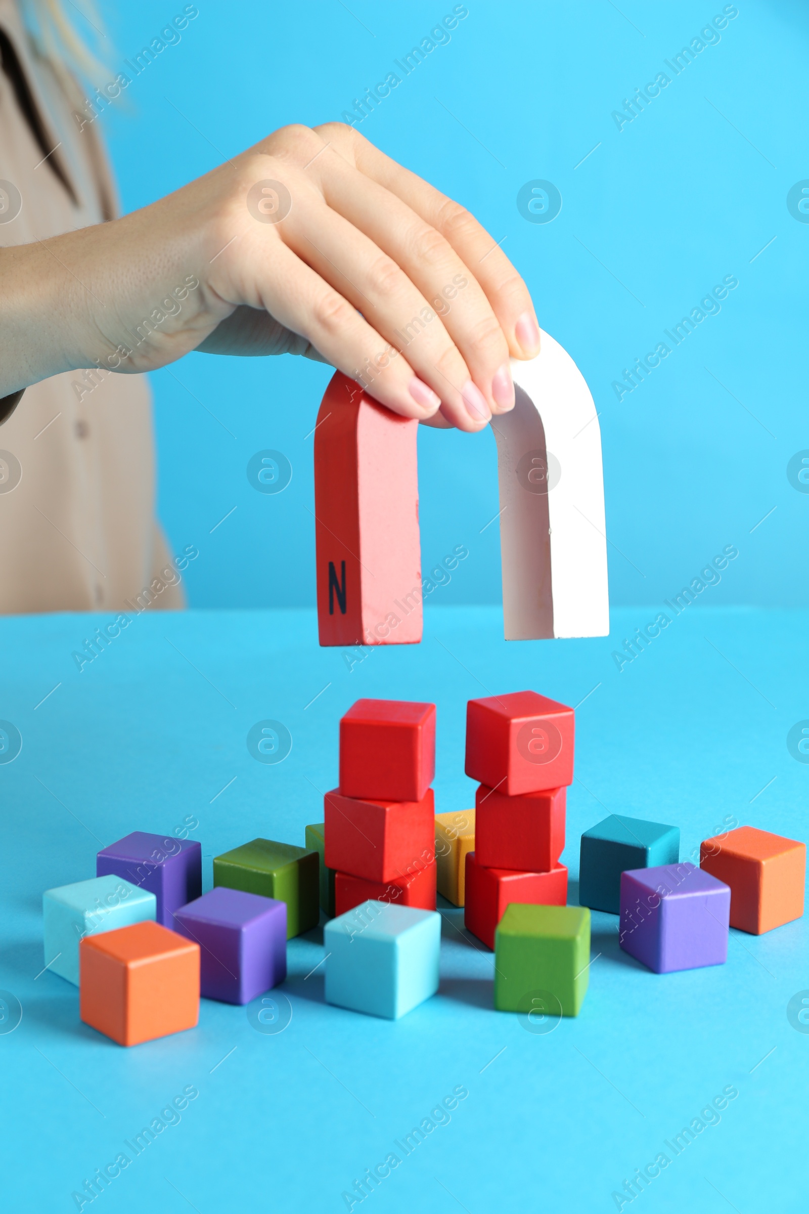 Photo of Woman with magnet attracting colorful cubes on light blue background, closeup