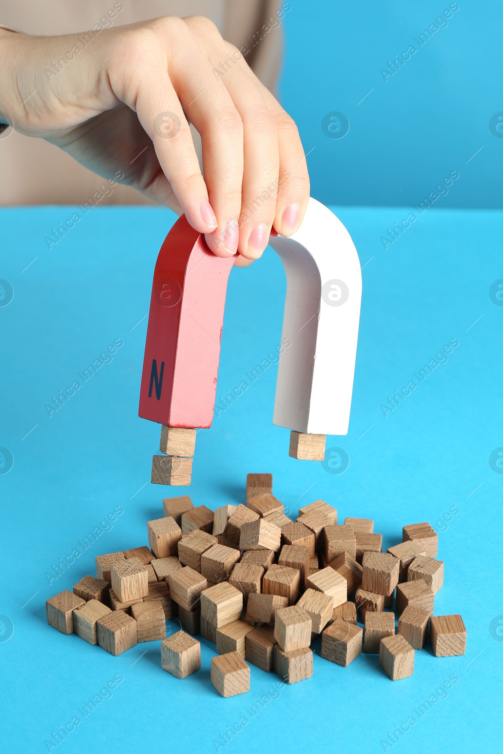 Photo of Woman with magnet attracting wooden cubes on light blue background, closeup