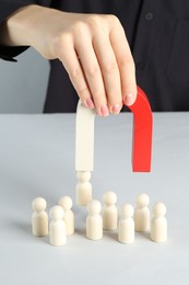 Photo of Woman with magnet attracting piece among wooden ones at white table, closeup