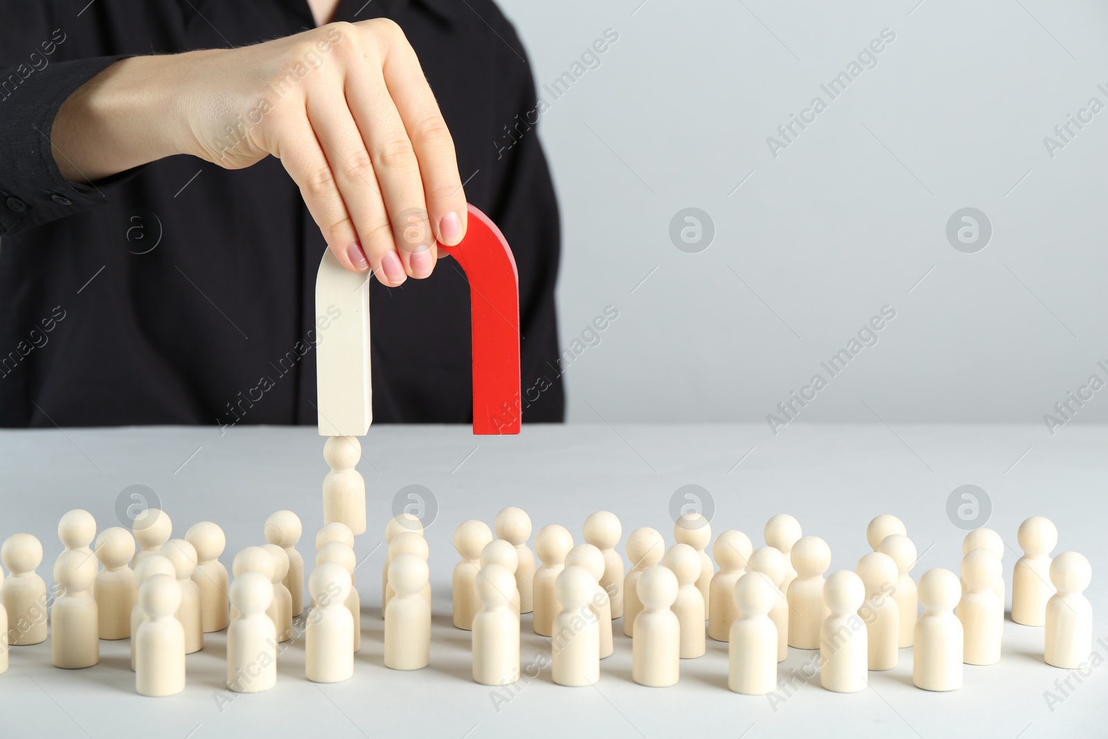 Photo of Woman with magnet attracting piece among wooden ones at white table, closeup