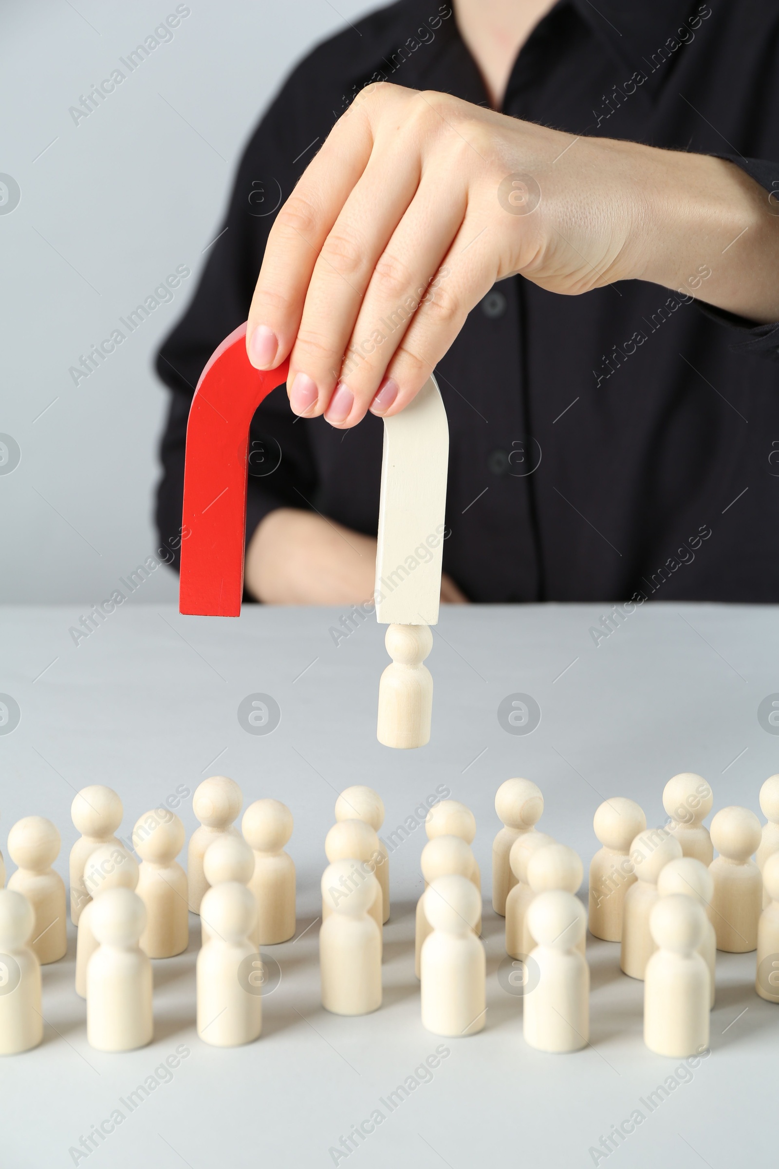 Photo of Woman with magnet attracting piece among wooden ones at white table, closeup