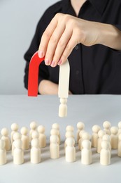 Photo of Woman with magnet attracting piece among wooden ones at white table, closeup