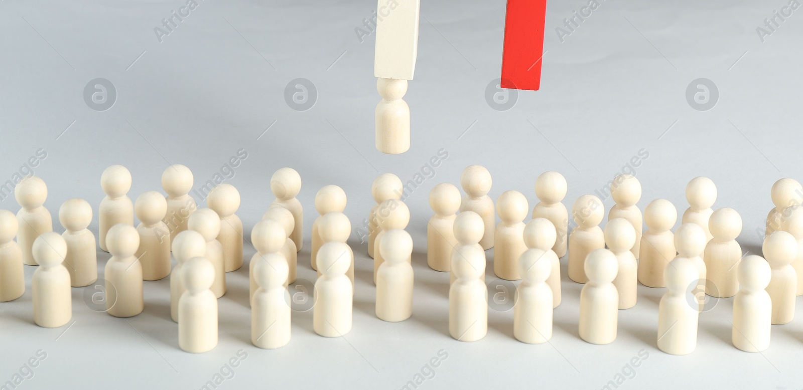 Photo of Attracting wooden human figures with magnet on white background, closeup