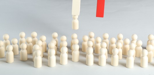 Photo of Attracting wooden human figures with magnet on white background, closeup