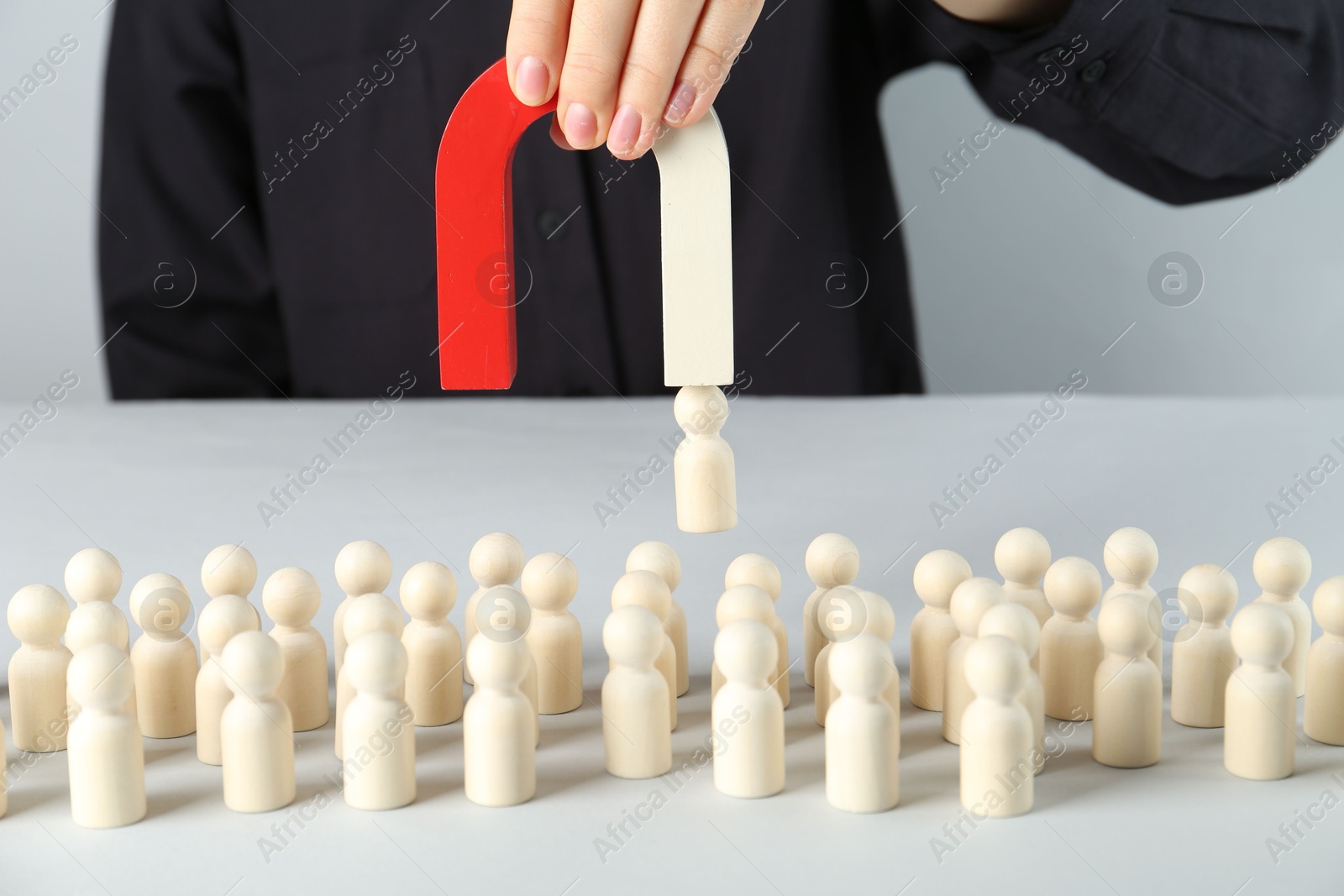 Photo of Woman with magnet attracting piece among wooden ones at white table, closeup