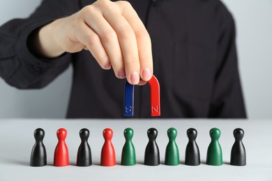 Photo of Woman with magnet attracting different game pieces at white table, closeup