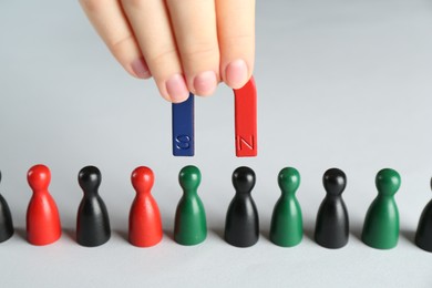 Photo of Woman with magnet attracting different game pieces at white table, closeup