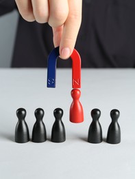 Photo of Woman with magnet attracting red piece among black ones at white table, closeup