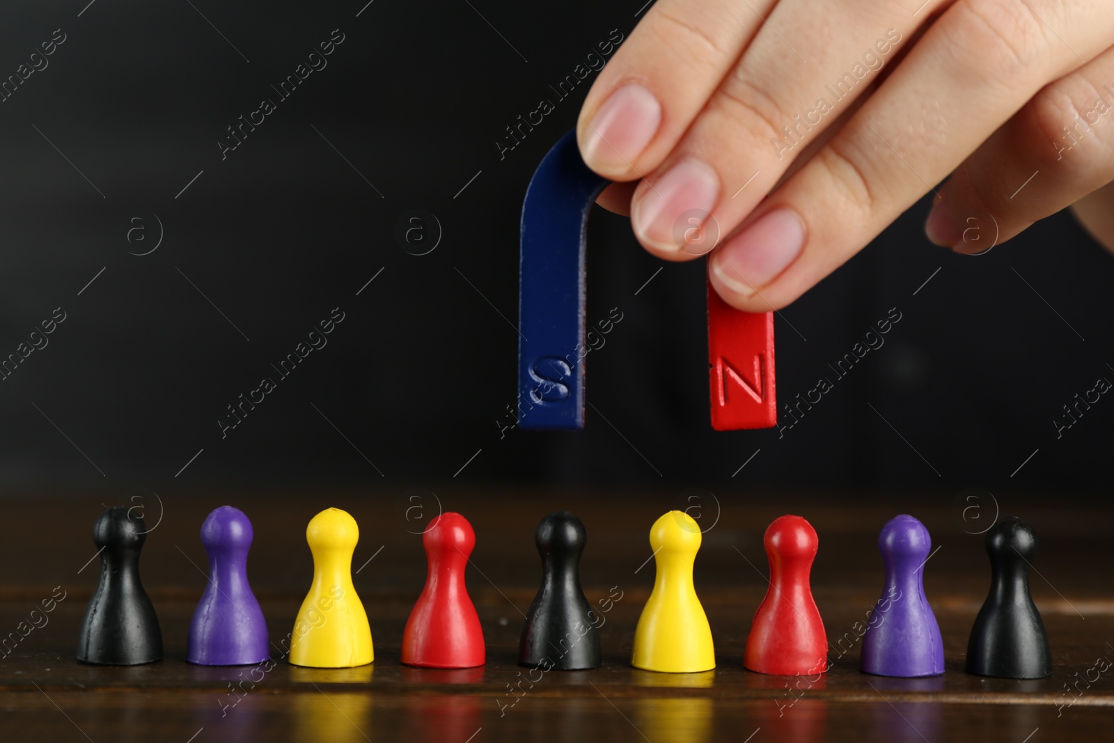 Photo of Woman with magnet attracting different game pieces at wooden table, closeup