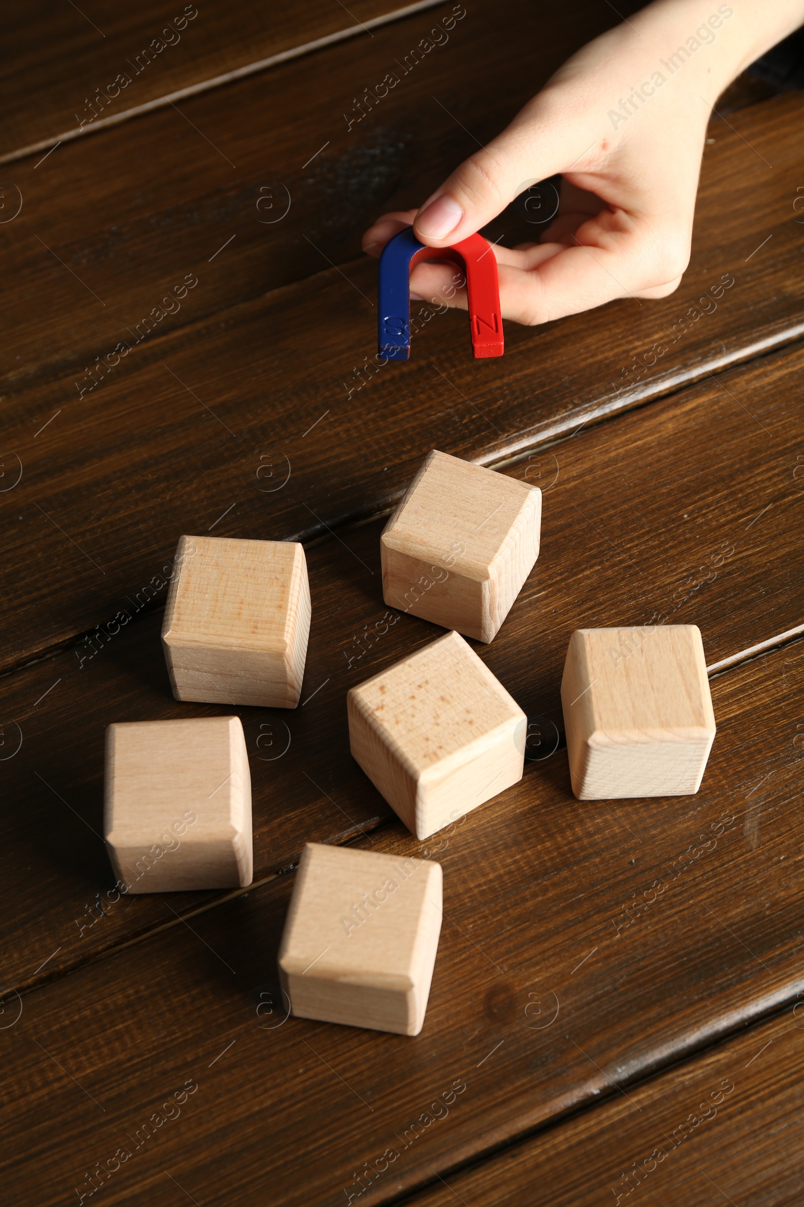 Photo of Woman with magnet attracting cubes at wooden table, closeup