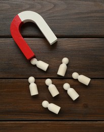 Photo of Magnet attracting human figures on wooden table, flat lay