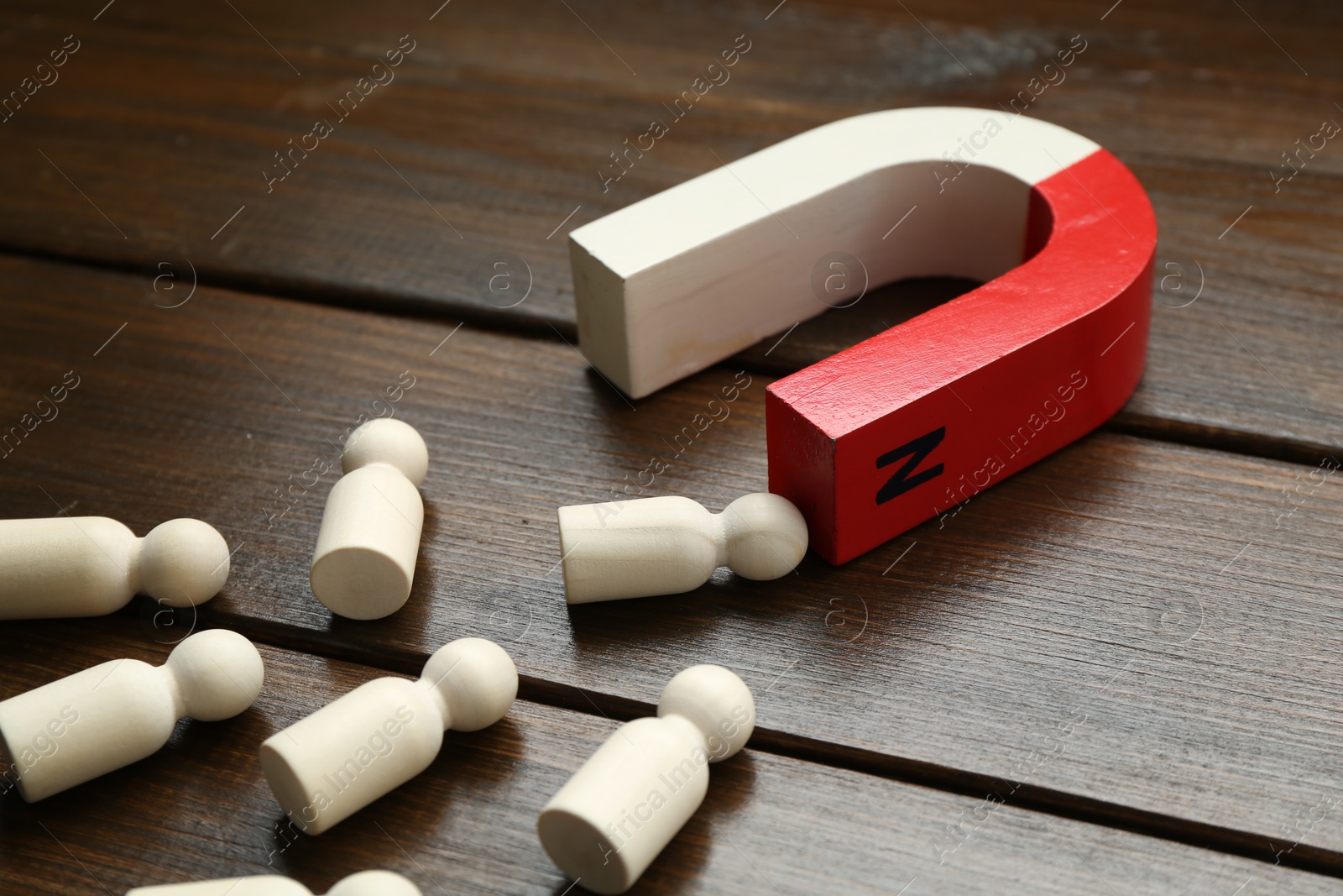 Photo of Magnet attracting human figures on wooden table, closeup