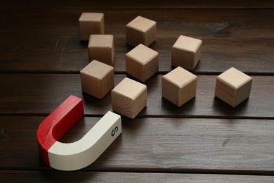 Photo of Magnet attracting cubes on wooden table, closeup