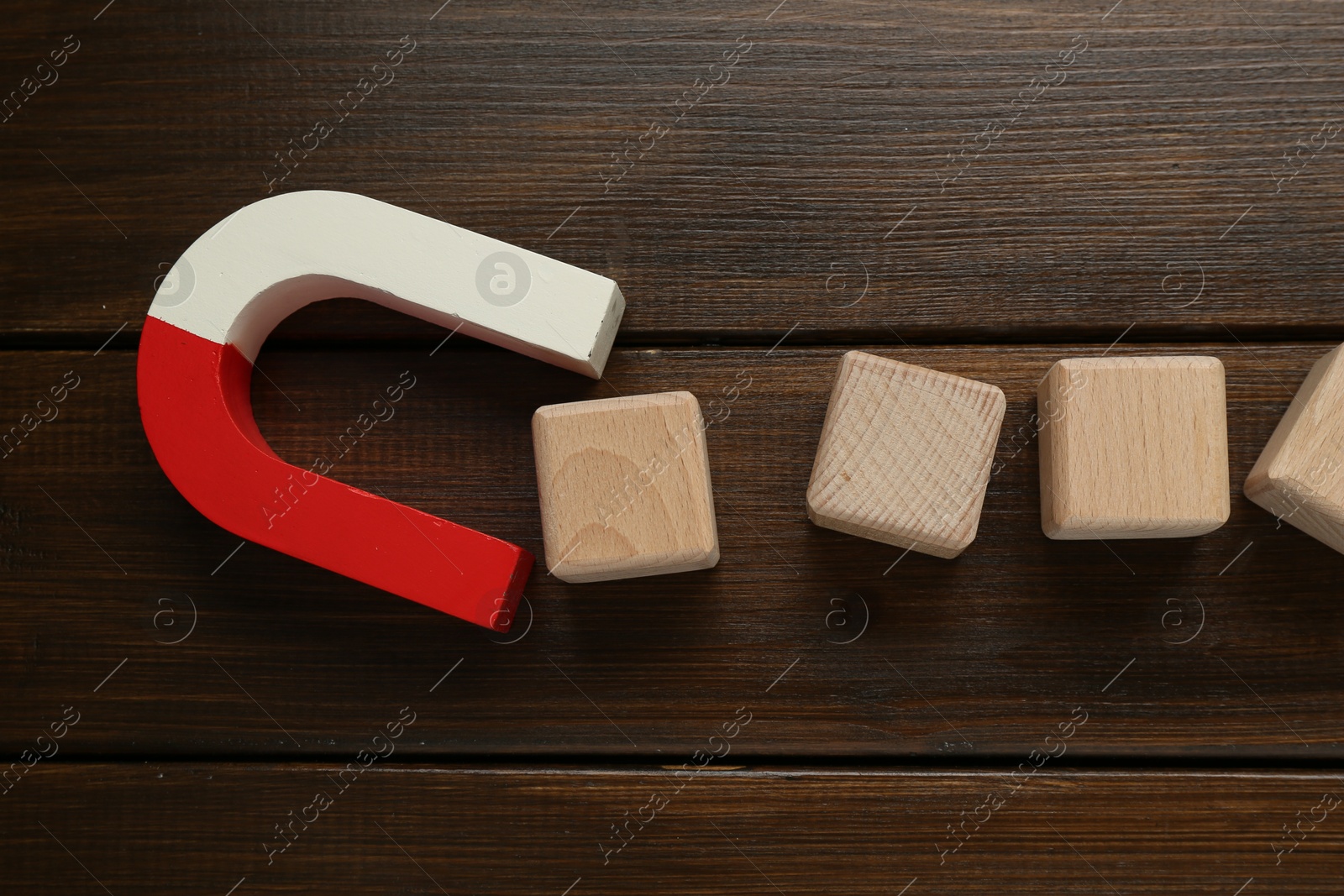 Photo of Magnet attracting cubes on wooden table, flat lay