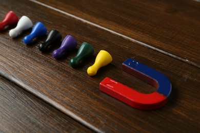 Photo of Magnet attracting colorful game pieces on wooden table, closeup