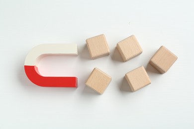 Photo of Magnet attracting wooden cubes on white background, flat lay