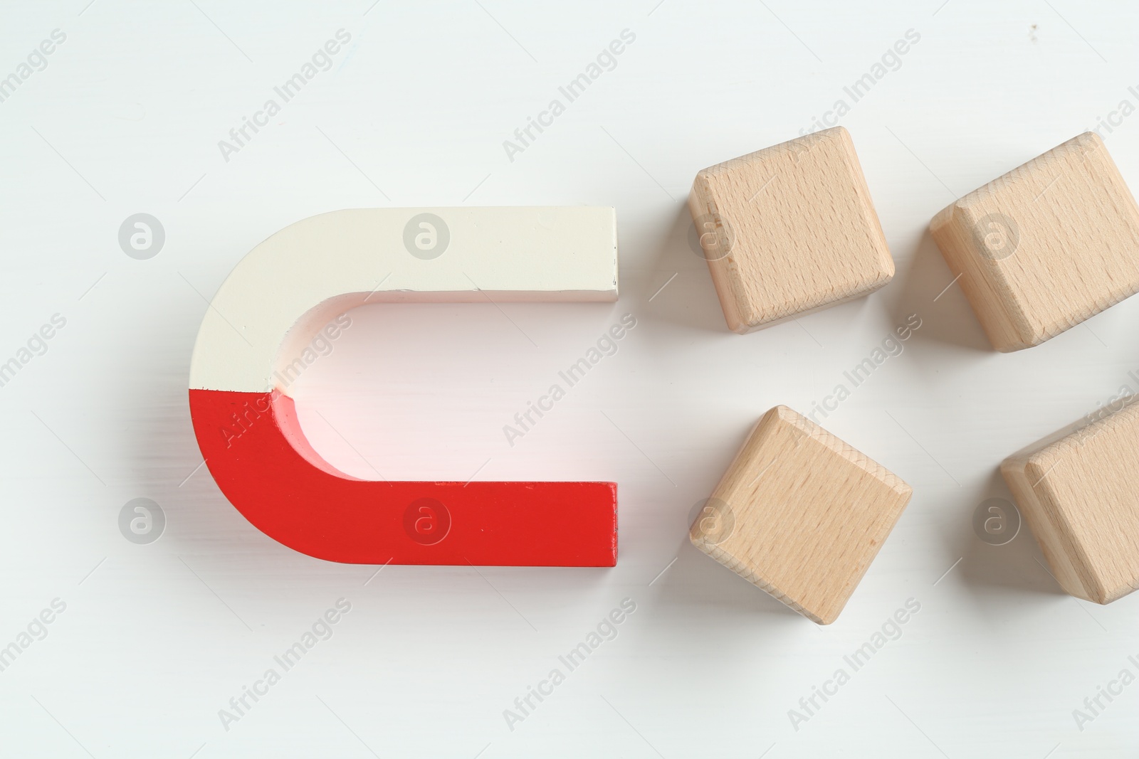 Photo of Magnet attracting wooden cubes on white background, flat lay