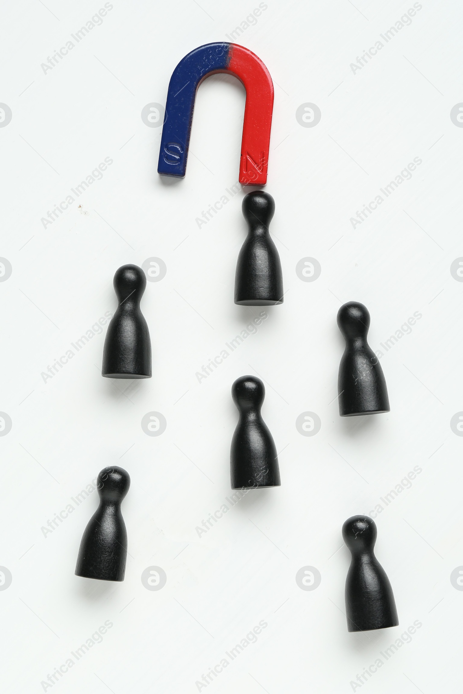 Photo of Magnet attracting black game pieces on white background, flat lay