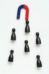 Photo of Magnet attracting black game pieces on white background, flat lay