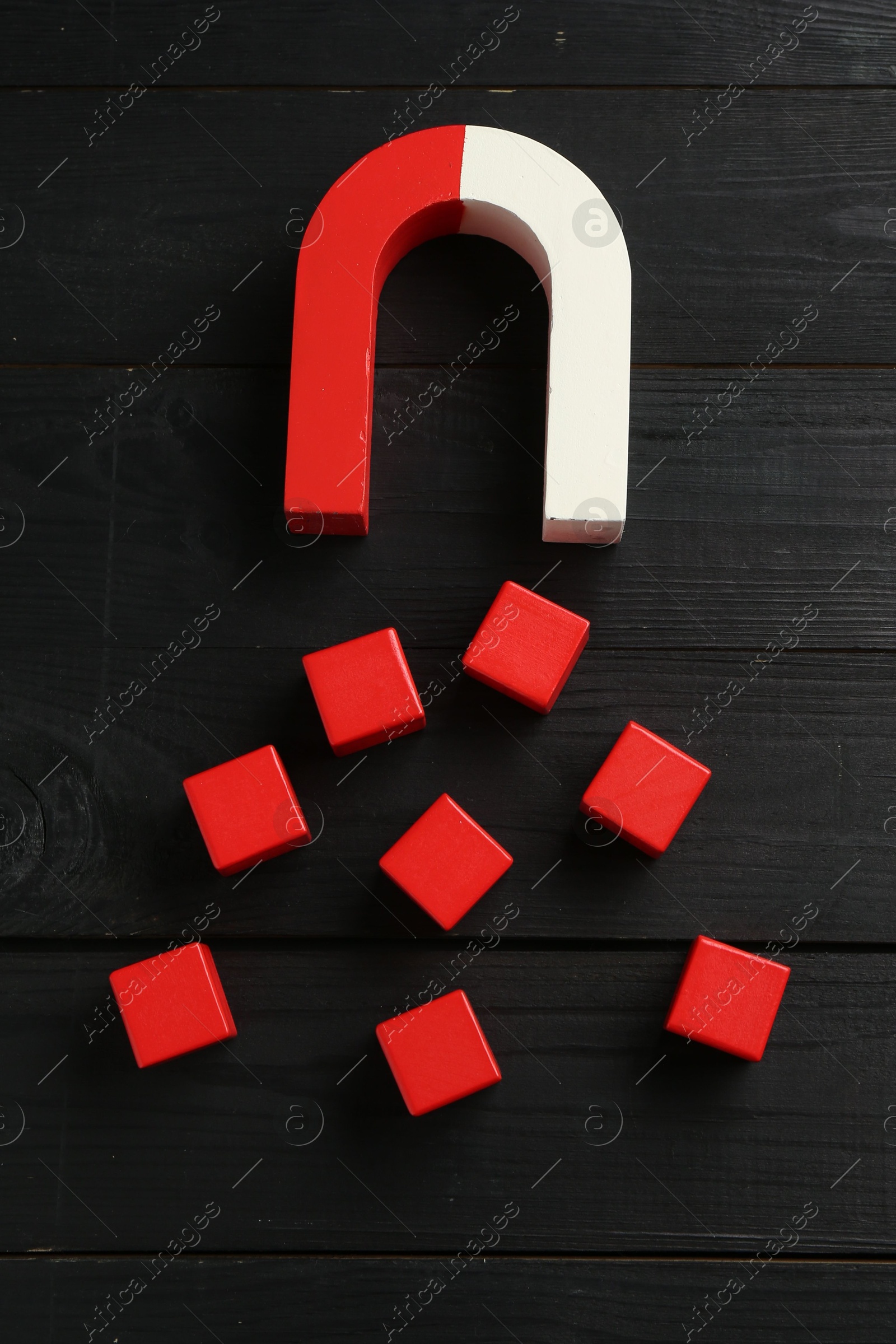 Photo of Magnet attracting red cubes on black wooden table, above view