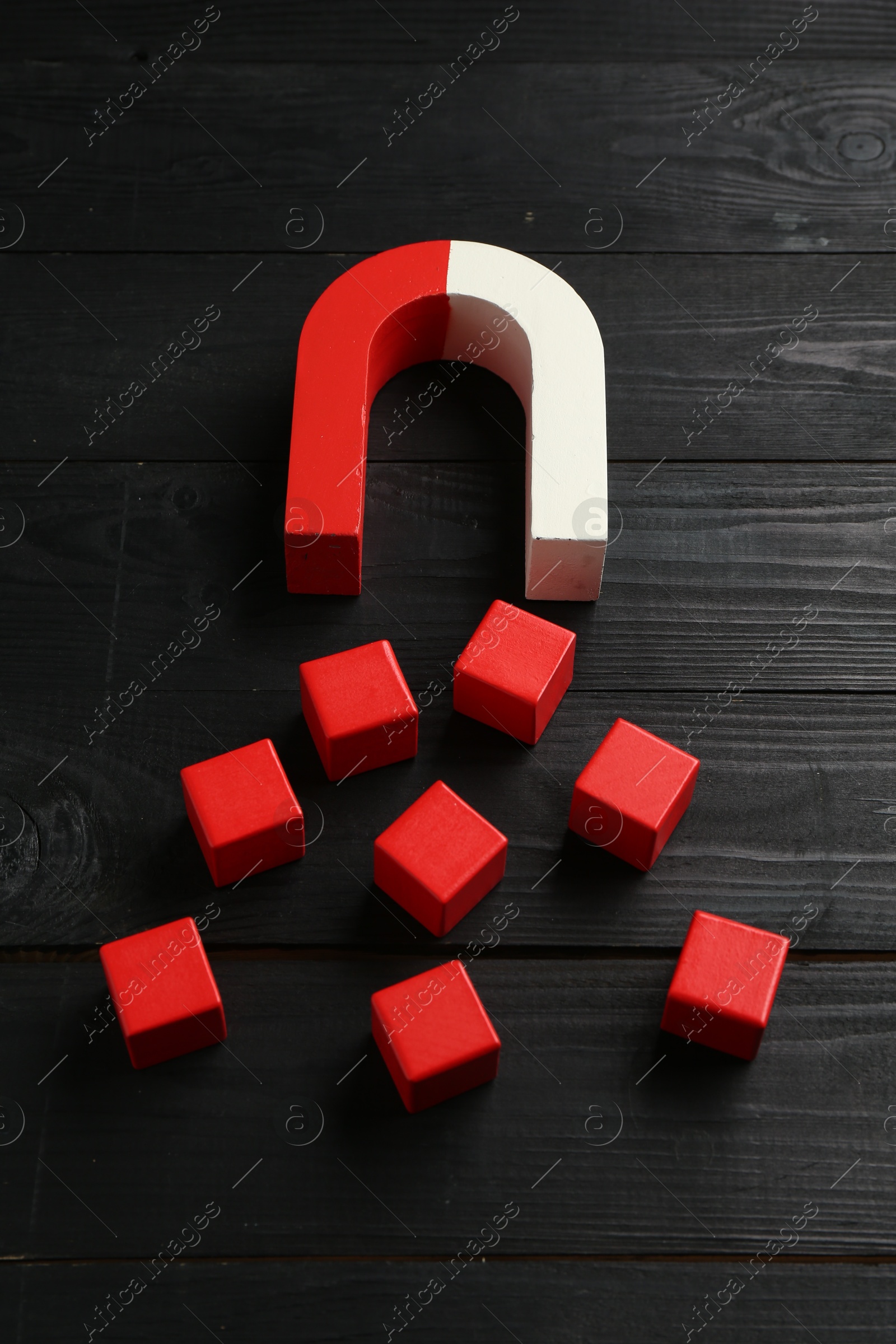 Photo of Magnet attracting red cubes on black wooden table