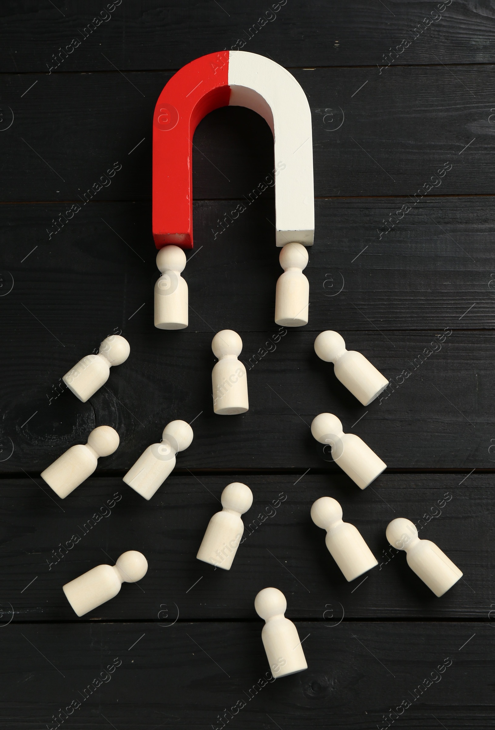 Photo of Magnet attracting human figures on black wooden table, above view