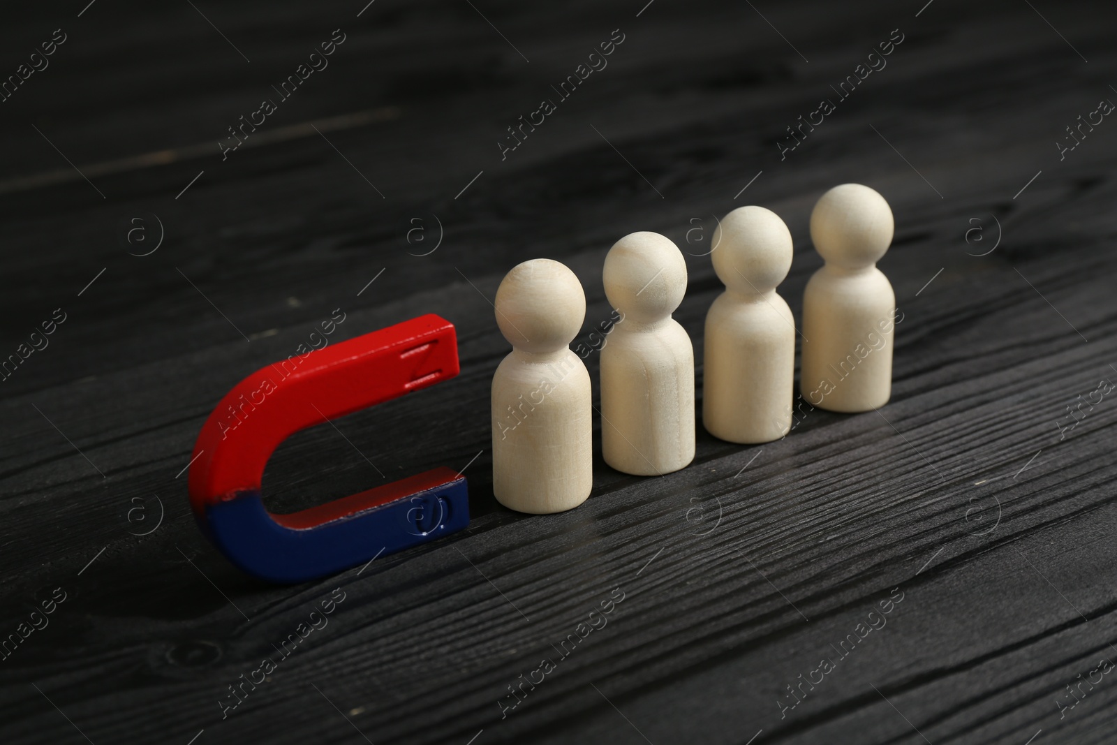 Photo of Magnet attracting human figures on black wooden table