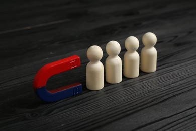 Photo of Magnet attracting human figures on black wooden table