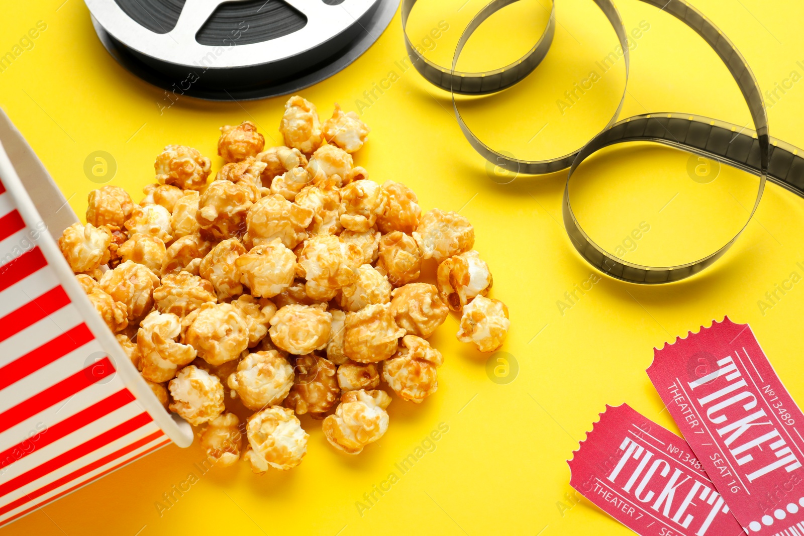 Photo of Movie tickets, sweet popcorn and film reel on yellow background, closeup