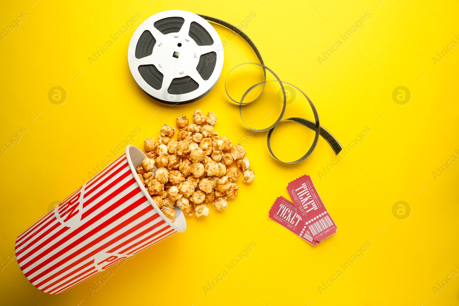 Photo of Movie tickets, sweet popcorn and film reel on yellow background, flat lay