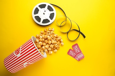 Photo of Movie tickets, sweet popcorn and film reel on yellow background, flat lay