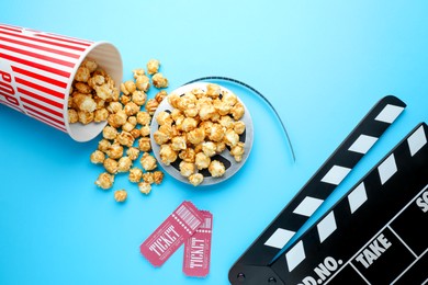 Movie clapper, sweet popcorn, tickets and film reel on light blue background, flat lay