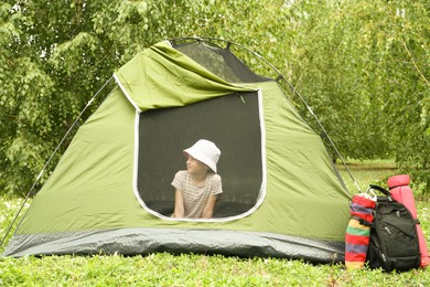 Girl sitting in camping tent on green grass outdoors