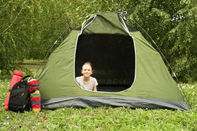 Girl sitting in camping tent on green grass outdoors