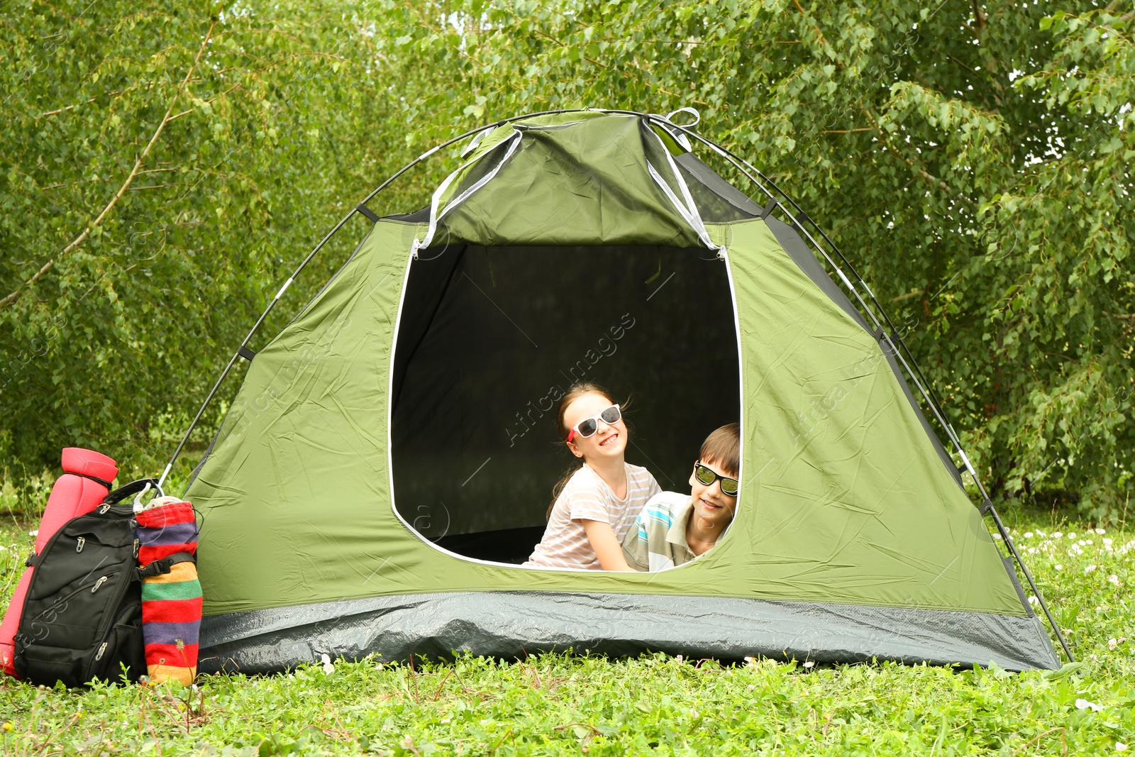 Photo of Girl and her brother resting in camping tent on green grass outdoors