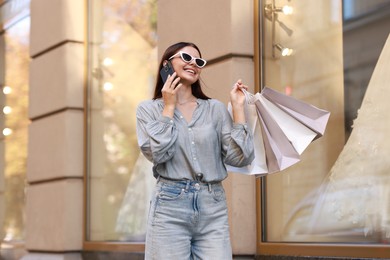 Photo of Happy woman with shopping bags talking on smartphone outdoors