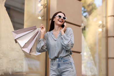 Photo of Happy woman with shopping bags talking on smartphone outdoors