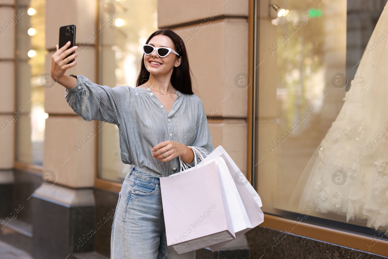 Photo of Happy woman with shopping bags taking selfie outdoors